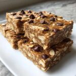 A stack of chewy, homemade protein bars made with oats and topped with chocolate chips.