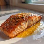 A perfectly cooked, glazed fillet of air fryer salmon seasoned with herbs, resting in its juices on a white plate.