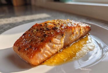 A perfectly cooked, glazed fillet of air fryer salmon seasoned with herbs, resting in its juices on a white plate.
