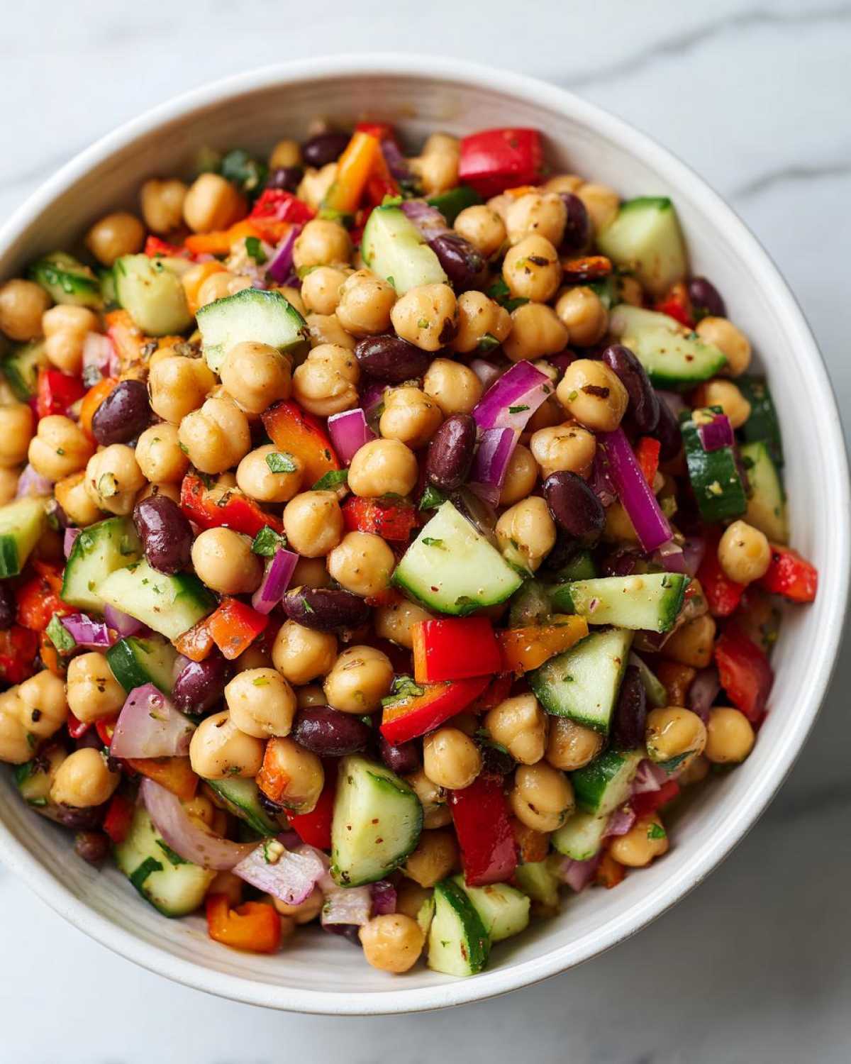 Close-up of a vibrant bowl of bean salad featuring chickpeas, kidney beans, cucumber, and red onion.