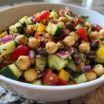 A vibrant bowl of fresh bean salad featuring chickpeas, black beans, cucumber, red onion, and bell peppers.