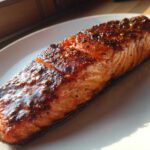 A perfectly cooked, glazed salmon fillet resting on a white plate, glistening under natural light.