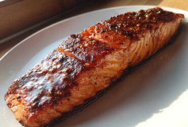 A perfectly cooked, glazed salmon fillet resting on a white plate, glistening under natural light.