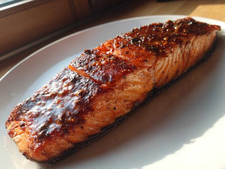 A perfectly cooked, glazed salmon fillet resting on a white plate, glistening under natural light.