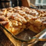 Close-up of a golden brown apple cobbler recipe baked in a clear glass dish, showing the crumb topping and cooked apple filling.