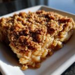 Close-up of a warm slice of apple crisp recipe showing gooey apples and a crunchy oat topping.