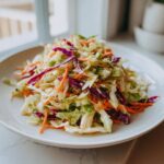A vibrant plate of homemade cabbage salad featuring shredded green cabbage, red cabbage, and carrots tossed in dressing.