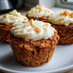 Close-up of four delicious carrot cake muffins topped with thick cream cheese frosting and carrot zest.