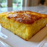 A close-up, featured image of a golden-brown slice of moist cornbread casserole on a white plate.