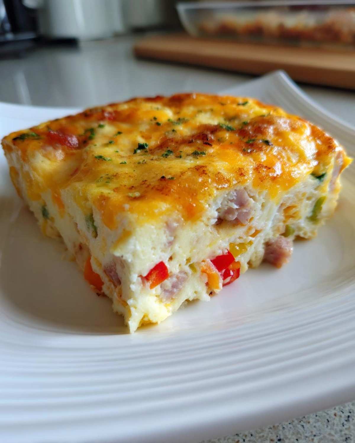 A thick, golden slice of savory egg bake featuring ham, colorful peppers, and melted cheese topping.