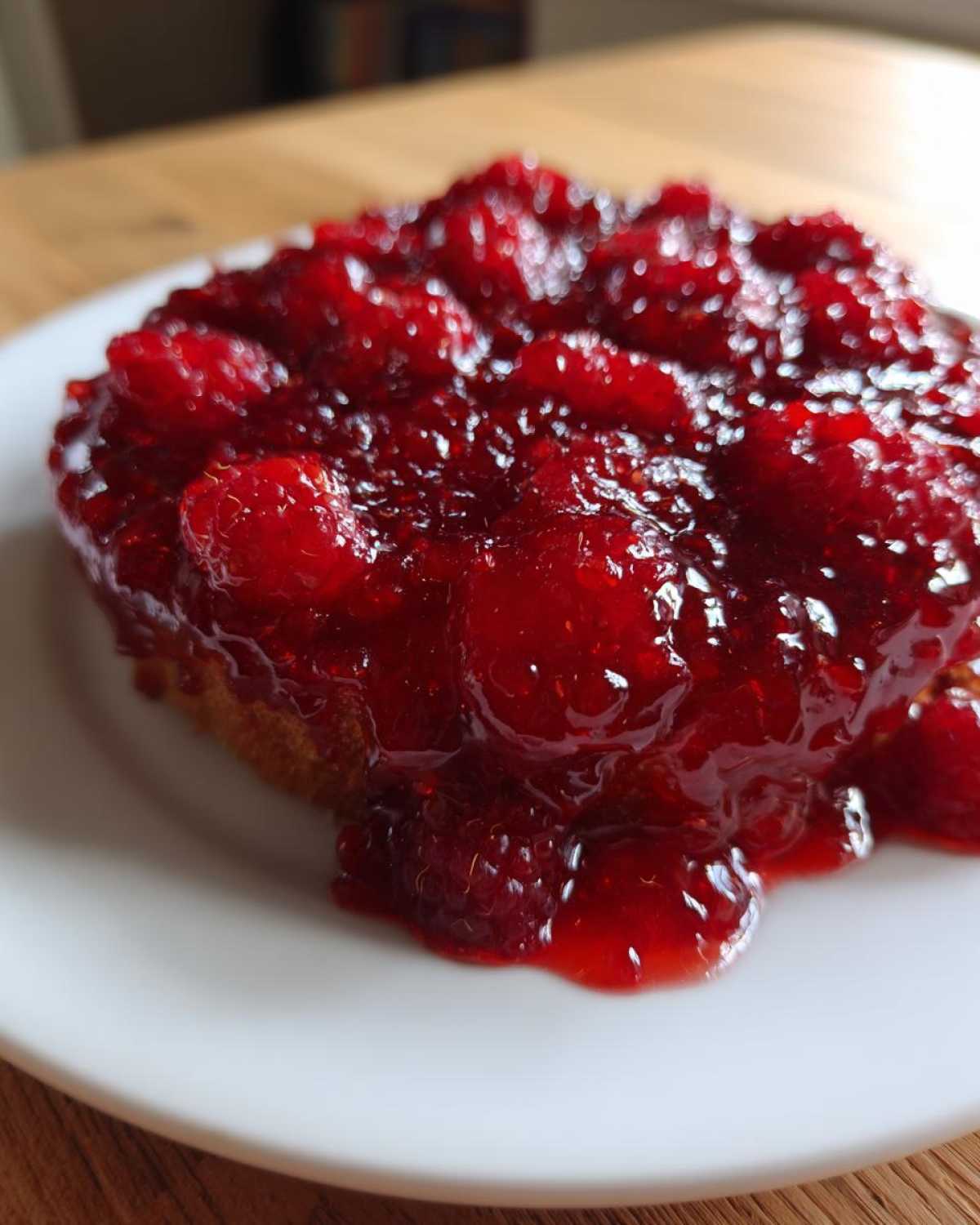 Close-up of thick, glossy homemade raspberry jam generously spread over a piece of toast on a white plate.