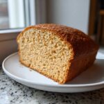 A close-up of a freshly baked loaf of whole wheat bread, showing its soft crumb, resting on a white plate.
