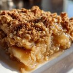 A close-up, mouthwatering shot of a square serving of apple crisp recipe showing warm, gooey filling and crunchy oat topping.