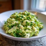A close-up of creamy avocado chicken salad mixed with chunks of white chicken meat and topped with fresh chopped parsley.