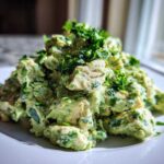 A mound of creamy avocado chicken salad mixed with fresh herbs, served on a white plate.