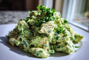 A mound of creamy avocado chicken salad mixed with fresh herbs, served on a white plate.
