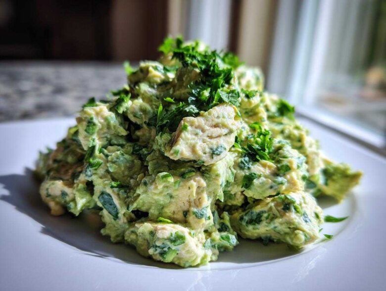 A mound of creamy avocado chicken salad mixed with fresh herbs, served on a white plate.