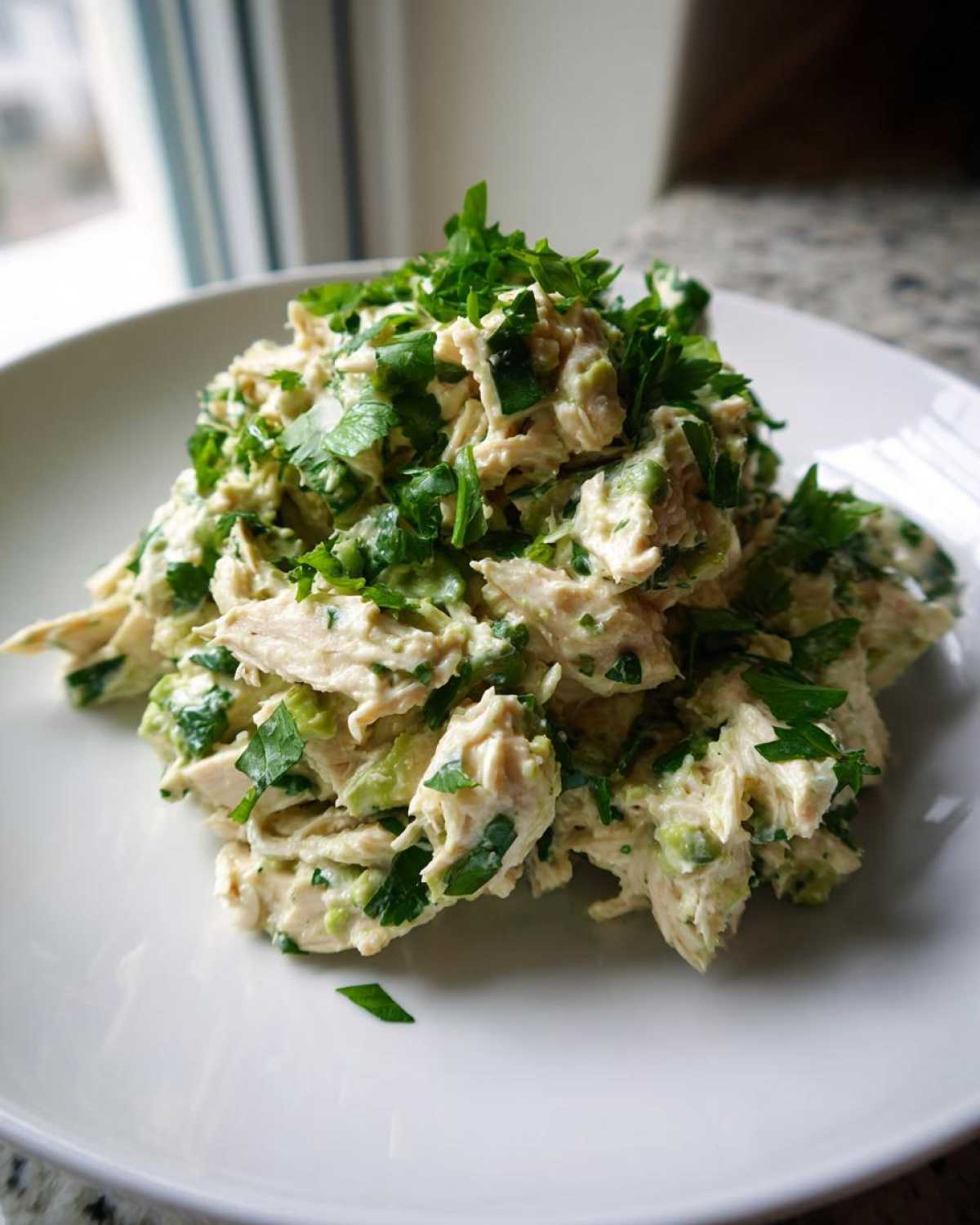 A generous mound of creamy avocado chicken salad topped with fresh chopped parsley on a white plate.