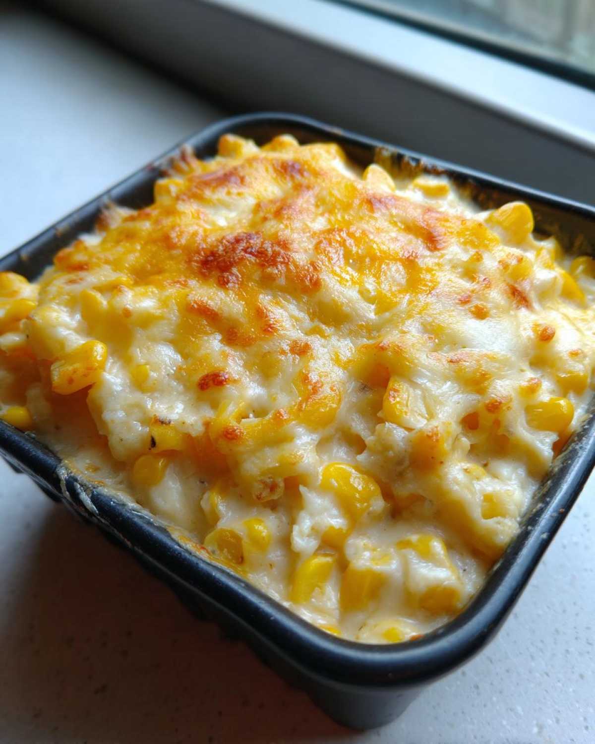 Close-up of a baked corn dip with cream cheese base, topped with bubbly, golden-brown melted cheese.