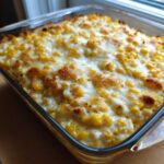 Close-up of a baked corn dip with cream cheese mixture, topped with melted and slightly browned cheese.