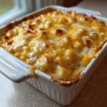 Close-up of a baked corn dip with cream cheese base topped with bubbly, browned cheddar cheese.