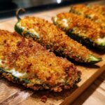 Close-up of golden brown baked jalapeño poppers stuffed with cream cheese and covered in crispy breadcrumbs.