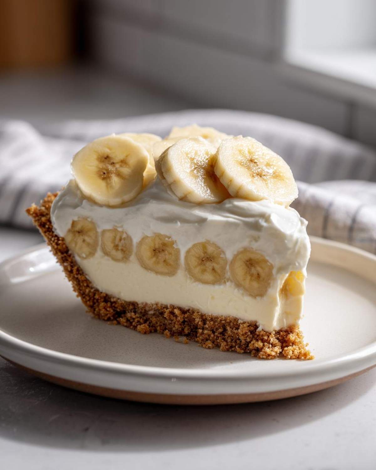 A perfect slice of banana cream pie recipe featuring a graham cracker crust, vanilla filling, and fresh banana slices topped with whipped cream.