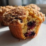 A close-up, cross-section view of a moist blueberry muffin with a sugary crumb topping, showing juicy blueberries inside.