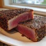 Two thick halves of a perfectly seared Blackened Tuna Steak showing a rare, pink center on a white plate.
