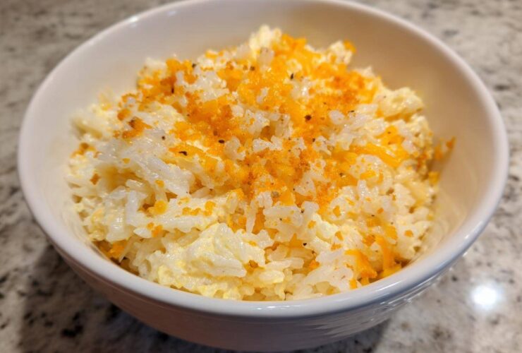 A white bowl filled with creamy, cheesy rice topped with bright orange shredded cheese and pepper.