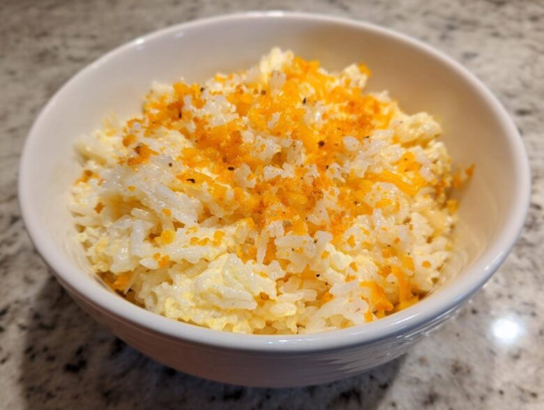 A white bowl filled with creamy, cheesy rice topped with bright orange shredded cheese and pepper.