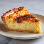 A close-up shot of a slice of creamy buttermilk pie resting on a light plate.