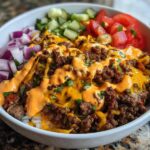 A close-up of a fully loaded cheeseburger bowl featuring seasoned ground beef, melted cheese, special sauce, and fresh toppings.