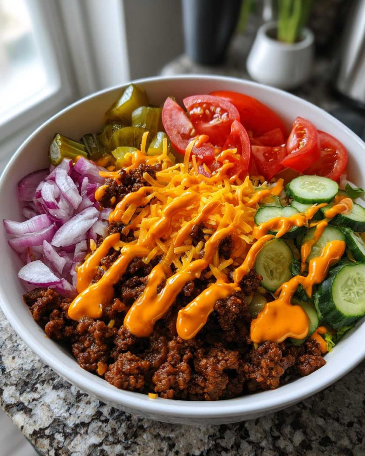 A close-up view of a fully assembled cheeseburger bowl featuring seasoned ground beef, shredded cheese, and fresh toppings.