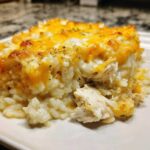 A close-up serving of creamy cheesy chicken and rice casserole topped with melted cheddar.