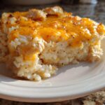 A serving of cheesy chicken and rice casserole topped with melted cheddar cheese on a white plate.