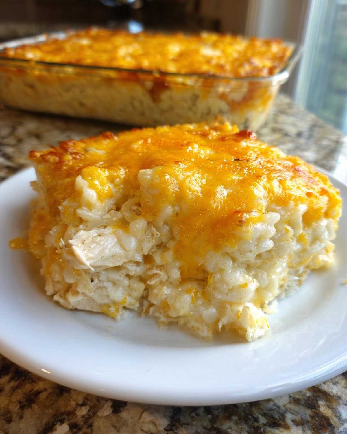 A square serving of creamy, cheesy chicken and rice casserole topped with melted cheddar cheese.