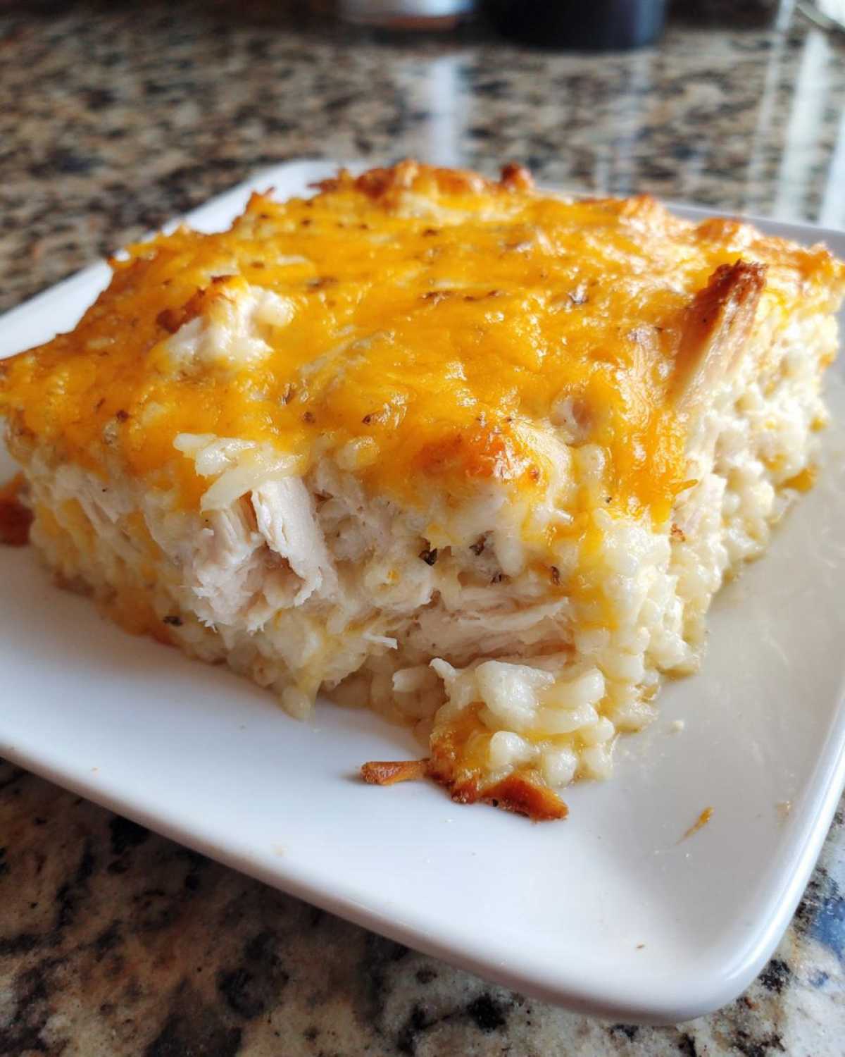 A square serving of cheesy chicken and rice casserole topped with melted cheddar cheese.
