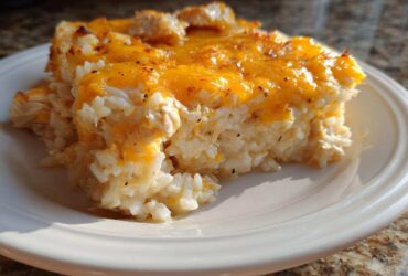 A serving of cheesy chicken and rice casserole topped with melted cheddar cheese on a white plate.