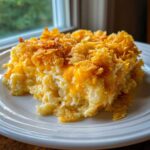 A scoop of creamy, cheesy potato casserole topped with melted cheddar cheese and crunchy cornflakes.