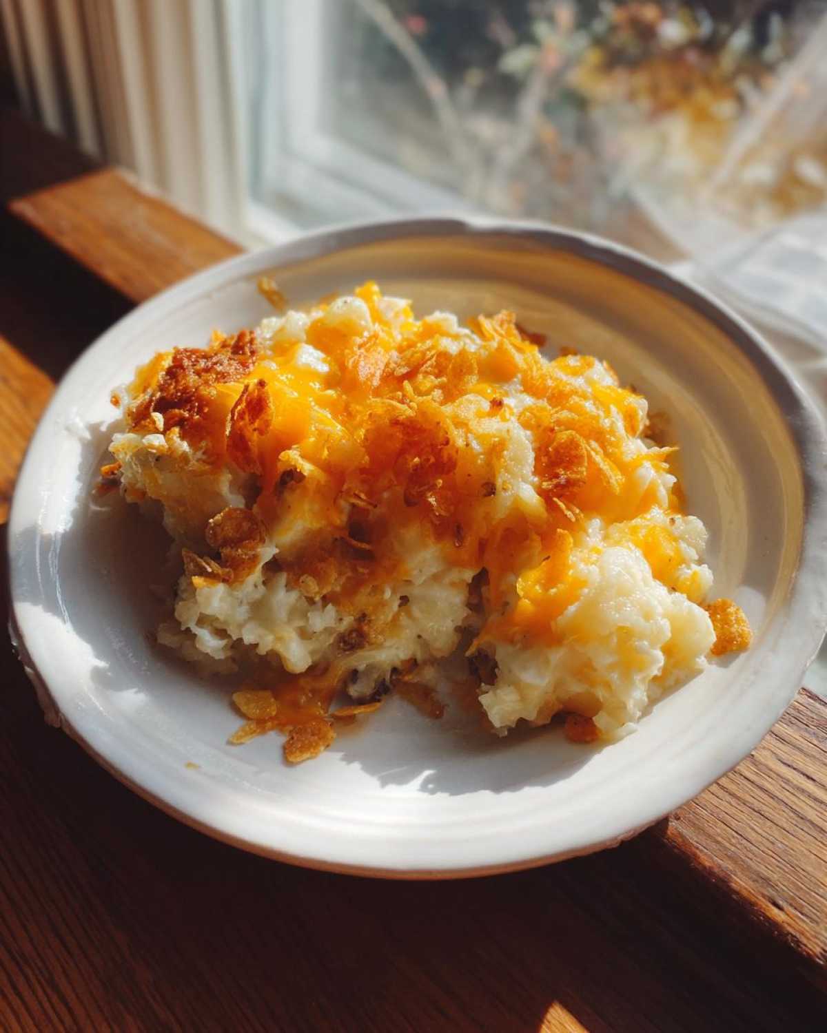 A scoop of creamy, cheesy potato casserole topped with melted cheddar and crispy cornflakes, served in a white bowl.