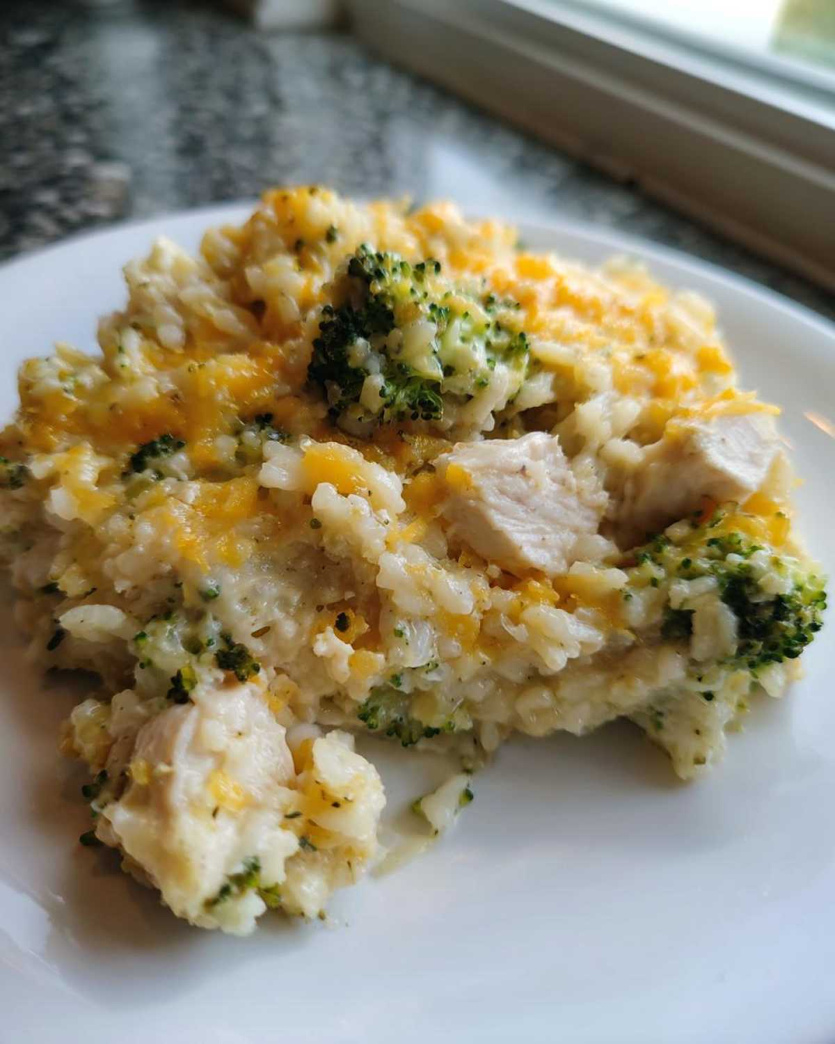 Close-up of a serving of creamy chicken broccoli rice casserole topped with melted cheddar cheese.