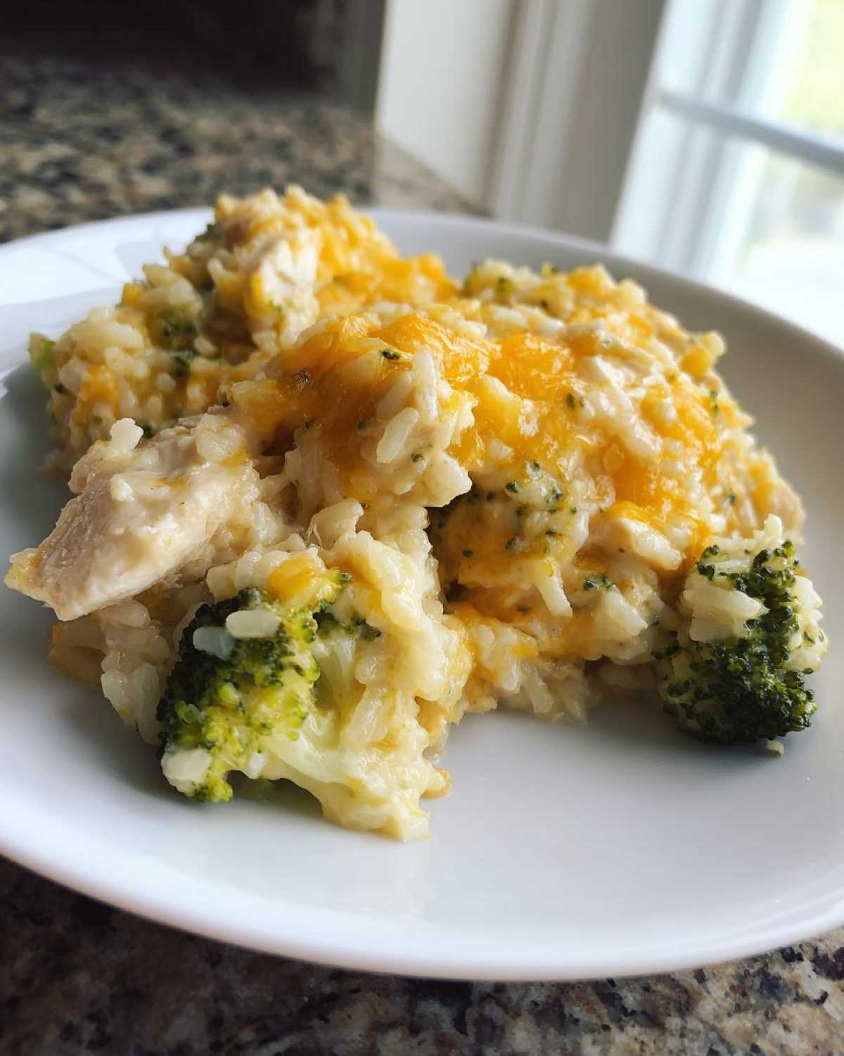 A scoop of creamy chicken broccoli rice casserole topped with melted cheddar cheese on a white plate.