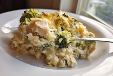 A spoonful of creamy chicken broccoli rice casserole topped with melted cheddar cheese being lifted from a white plate.