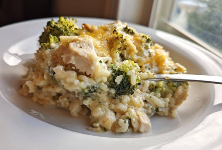 A spoonful of creamy chicken broccoli rice casserole topped with melted cheddar cheese being lifted from a white plate.