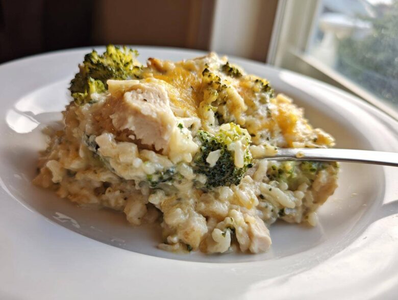 A spoonful of creamy chicken broccoli rice casserole topped with melted cheddar cheese being lifted from a white plate.