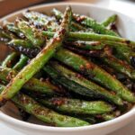 Close-up of blistered, glossy chinese green beans with garlic sauce in a white bowl.