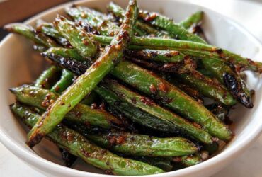 Close-up of blistered, glossy chinese green beans with garlic sauce in a white bowl.