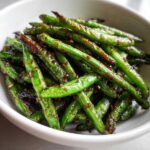 Close-up of vibrant green beans coated in a savory, dark chinese green beans with garlic sauce, served in a white bowl.