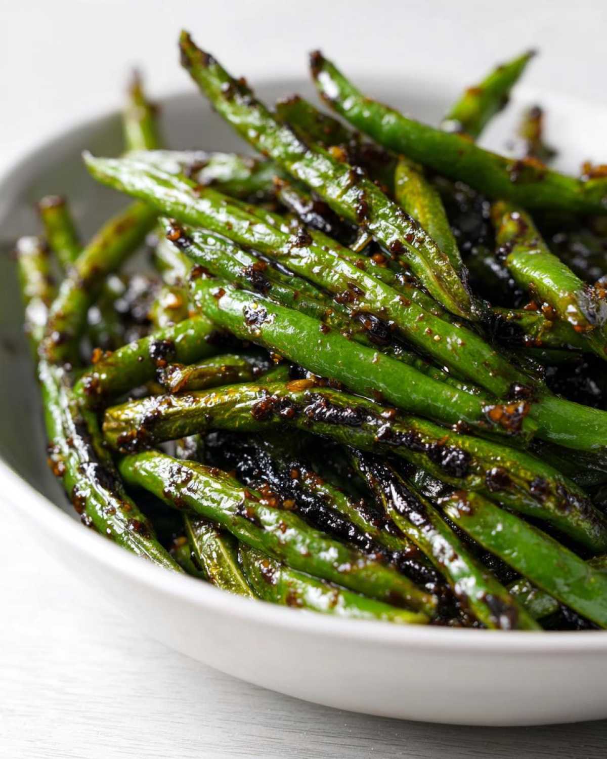 Close-up of vibrant green beans coated in a dark, glossy chinese green beans with garlic sauce.